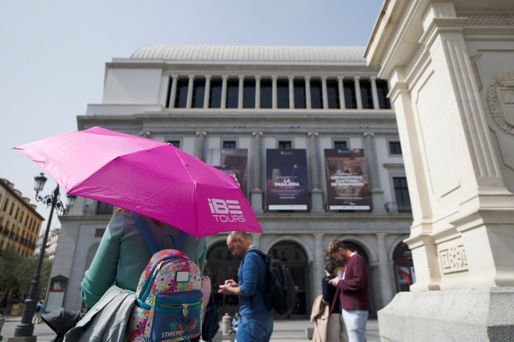 People with umbrellas near a large building with columns and banners.