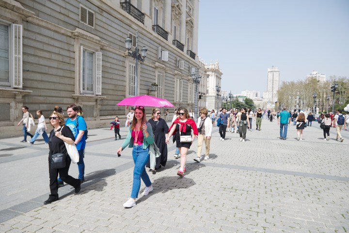People walking in an urban area, one holding a pink umbrella on a sunny day.