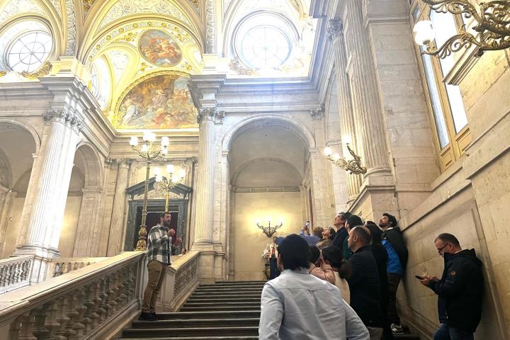 Group of people on grand staircase in ornate building with arched ceilings and chandeliers.
