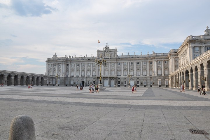 People walking in a large courtyard with a grand building in the background.