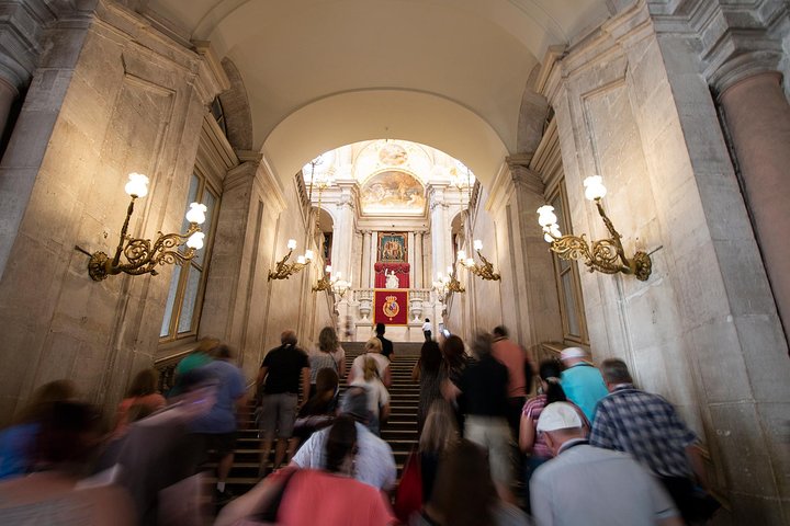 People ascending grand staircase with ornate lights and art.