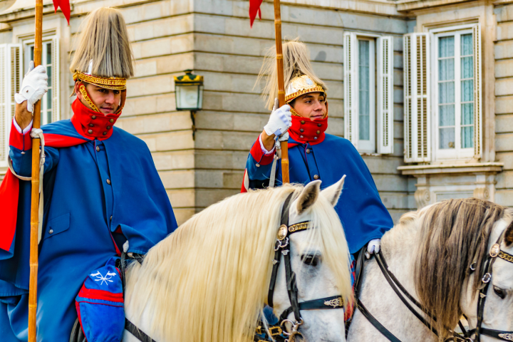 Two mounted guards in blue uniforms with tall hats and red accents outside a historic building.