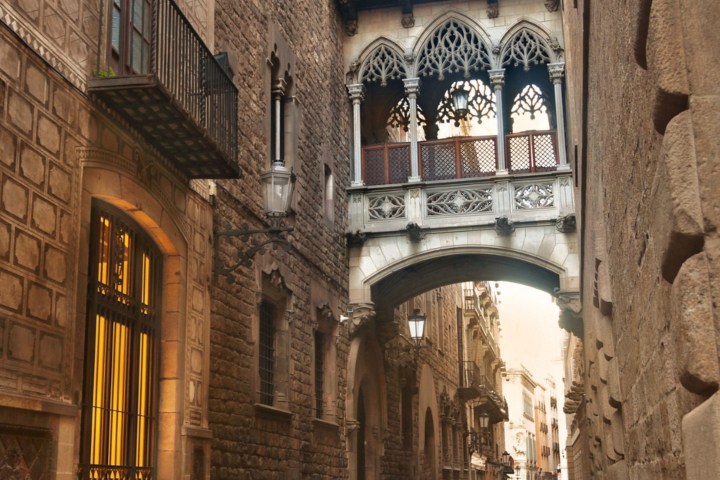 Gothic-style bridge over a narrow, wet cobblestone street between stone buildings.